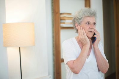 An older woman listens intently to a phone call, her expression tense and concerned.