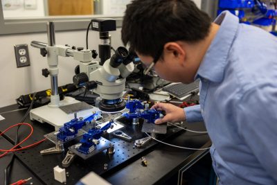 A man wearing a long-sleeved blue-shirt adjusts the clamps on a microchip.