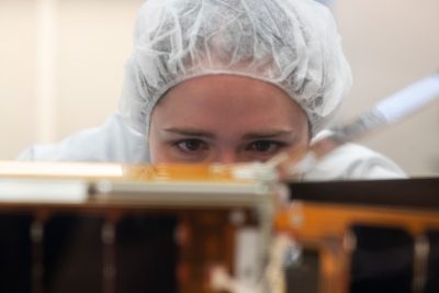 Woman wearing hair covering inspects a piece of equipment. 