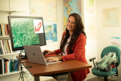 Woman in salmon colored sweater uses a laptop with mapping software