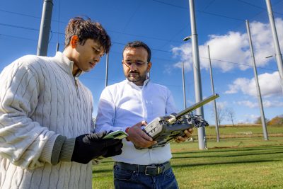 Grad students test wireless signal strength  for CCI outdoor testbed. Students are standing next to a large drone cage.