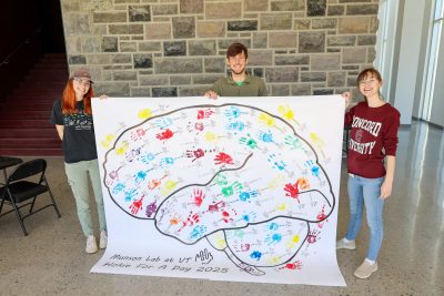 Students hold a large picture of a brain outline filled with colorful children's handprints