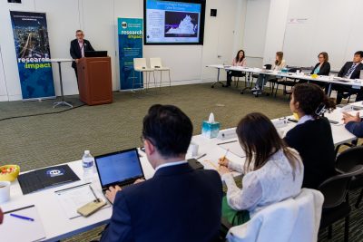CCI's Luiz DaSilva at the podium with people sitting at a u-shaped table.