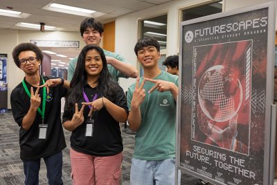 Students pose beside a Futurescapes student program display reading ‘Securing the Future, Together.