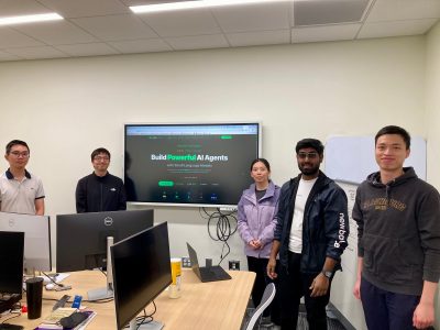 Five people stand in front of a computer screen