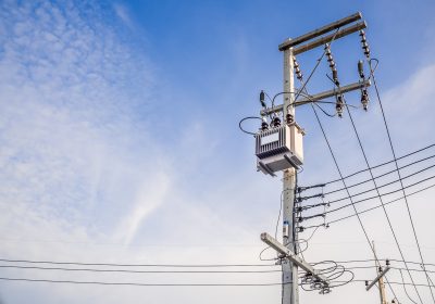 Electrical transformer mounted on a utility pole against a bright blue sky