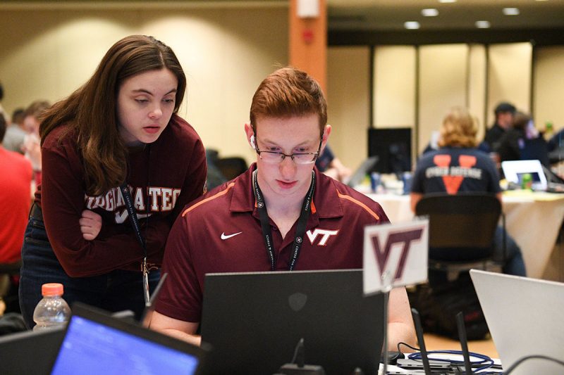 Two people wearing Virginia Tech gear focus intently on a laptop